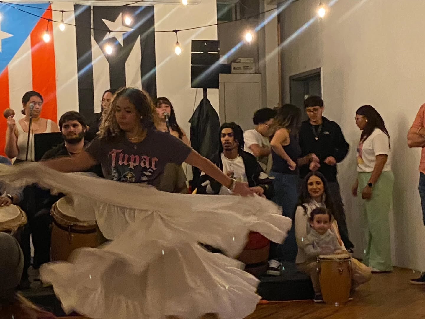 Bomba dancer in a flowing white skirt performing at El Batey while drummers and community watch / Bailarina de Bomba con falda blanca en El Batey
